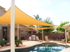 an outdoor pool with chairs and umbrellas next to the swimming pool in front of a house