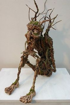 a sculpture made out of branches and twigs on top of a white surface with one foot in the air