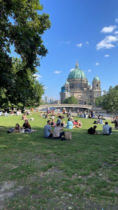 many people are sitting on the grass in front of a large building with a dome