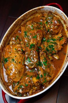 a red pot filled with meat covered in gravy and garnished with parsley