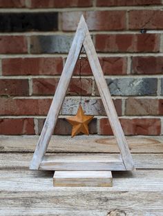 a wooden triangle with a star hanging from it's side on a table in front of a brick wall