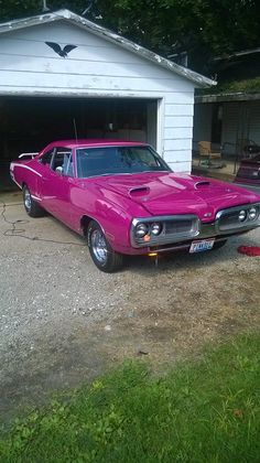 a pink muscle car parked in front of a garage with the door ajar open