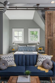 a blue couch sitting under two windows in a bedroom