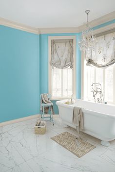 a white bath tub sitting next to a window in a blue and white bathroom with a chandelier hanging from the ceiling