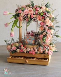 an arrangement of pink flowers and greenery on a wooden stand