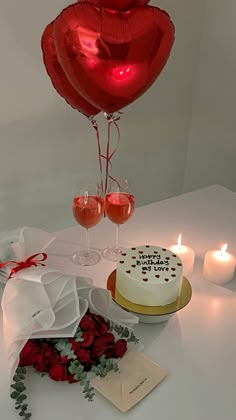 a cake and two wine glasses on a white table with red roses in the foreground