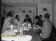 a group of people sitting at a table with drinks and papers on it, in a black and white photo