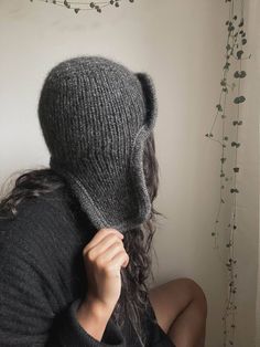 a woman wearing a gray knitted hat covering her face with the hood up and hands behind her head