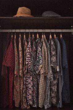 an open closet with clothes and hats hanging on the rack, all in different colors