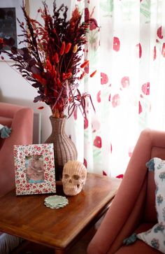 there is a vase with red flowers on the table next to two pictures and a skull