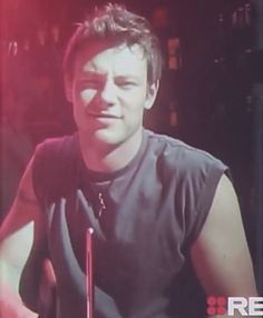 a man sitting in front of a microphone on top of a tv screen with red lights behind him