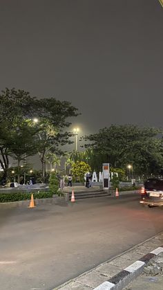 cars are driving down the road at night in an area with tall trees and street lights