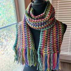 a multicolored crocheted scarf is on a mannequin in front of a window