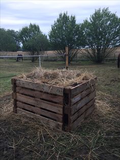 a wooden box filled with hay in the middle of a grass field next to a horse