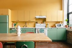 a kitchen with green and yellow cabinets, an oven, sink, microwave and table in it