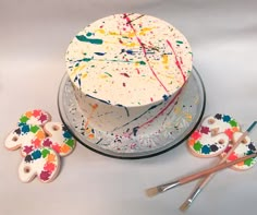 a cake with paint splattered on it and decorated cookies next to the cake