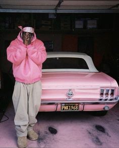 a person standing in front of a pink car talking on a cell phone while wearing a pink hoodie