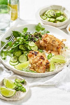 chicken with cucumbers and rice on a plate next to water, lemon wedges and lime slices