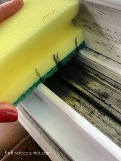 a hand holding a sponge over a window sill with black and yellow paint on it