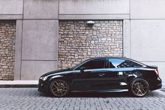 a black car parked in front of a stone building with gold rims on it