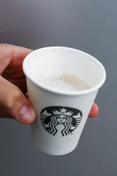 a hand holding a starbucks cup in front of a gray background