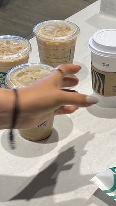 a woman's hand reaching for two cups of iced coffee on a white table