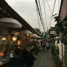 people are walking down an alley way with umbrellas over their heads and plants on the sidewalk