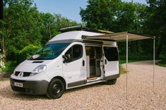 a small white van parked on top of a gravel road next to trees and bushes