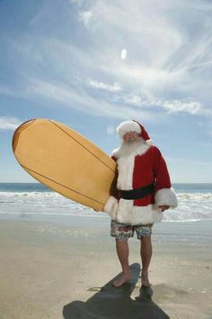 a man dressed as santa claus holding a surfboard on the beach