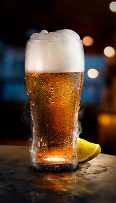 a close up of a glass of beer on a table with a slice of lime