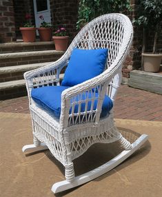 a white wicker rocking chair with blue cushions on the front patio area in front of a brick house