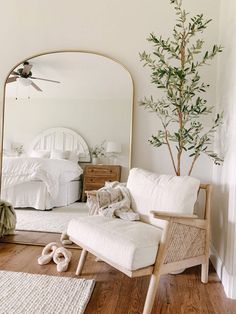 a living room with white furniture and a tree in the corner near a mirror that has been placed on the floor