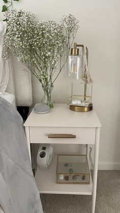 a bedside table with flowers on it and an alarm clock sitting next to it in front of a bed