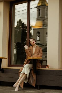 a woman sitting at a table in front of a window with her hand up to her face