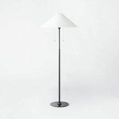 a floor lamp with a white shade on the top and black base, standing in front of a white background