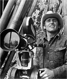 a man wearing a cowboy hat standing next to a camera