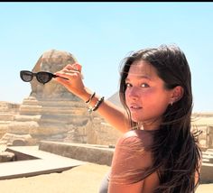 a woman holding up her sunglasses in front of an egyptian pyramid