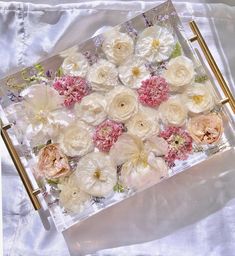 an arrangement of flowers in a clear box on a white table cloth with gold handles