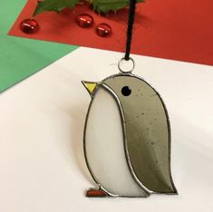 a glass penguin ornament hanging from a string on a white table with holly leaves