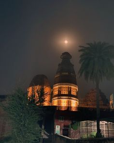 the moon is setting over an old building with palm trees in front of it on a foggy night