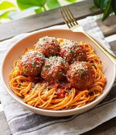 spaghetti with meatballs and parmesan cheese in a white bowl on a wooden table