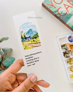 someone is holding up a bookmark with an image of a house and mountains on it