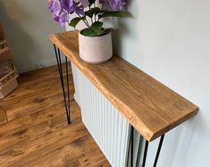 a vase with purple flowers sitting on top of a wooden shelf next to a wall