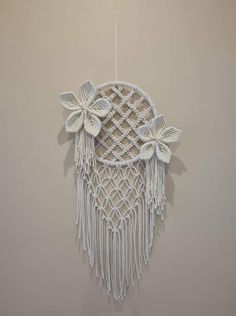 a macrame hanging on the wall decorated with flowers and leaves, made from white yarn