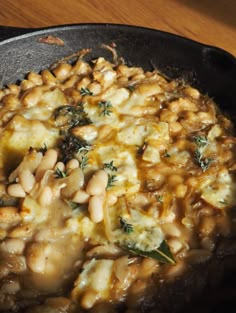 a skillet filled with beans and cheese on top of a wooden table next to a knife