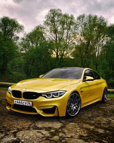 a yellow car is parked in the dirt near some trees and bushes on a cloudy day