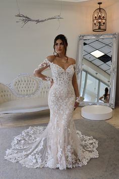 a woman standing in front of a mirror wearing a wedding dress with off the shoulder sleeves