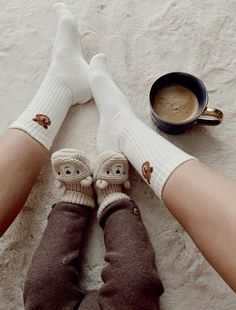 two people wearing white socks are sitting on the floor next to a cup of coffee