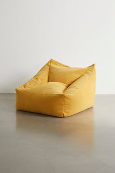 a yellow bean bag chair sitting on top of a cement floor next to a white wall