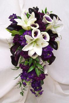 a bridal bouquet with purple and white flowers on a white cloth draped in the background